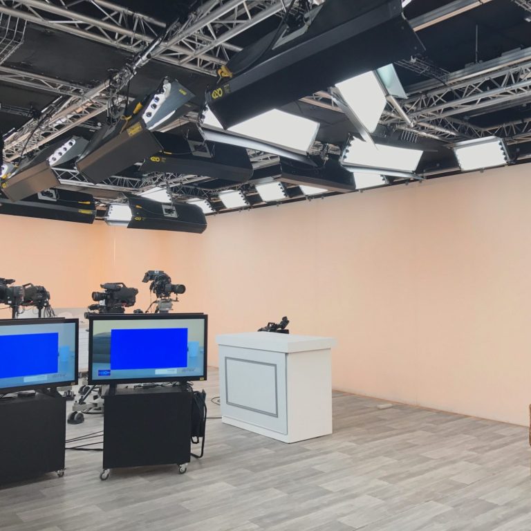 Studio de télévision avec plusieurs caméras et écrans, fond mural rétroéclairé CCT 2700°K / 6500°K IRC98